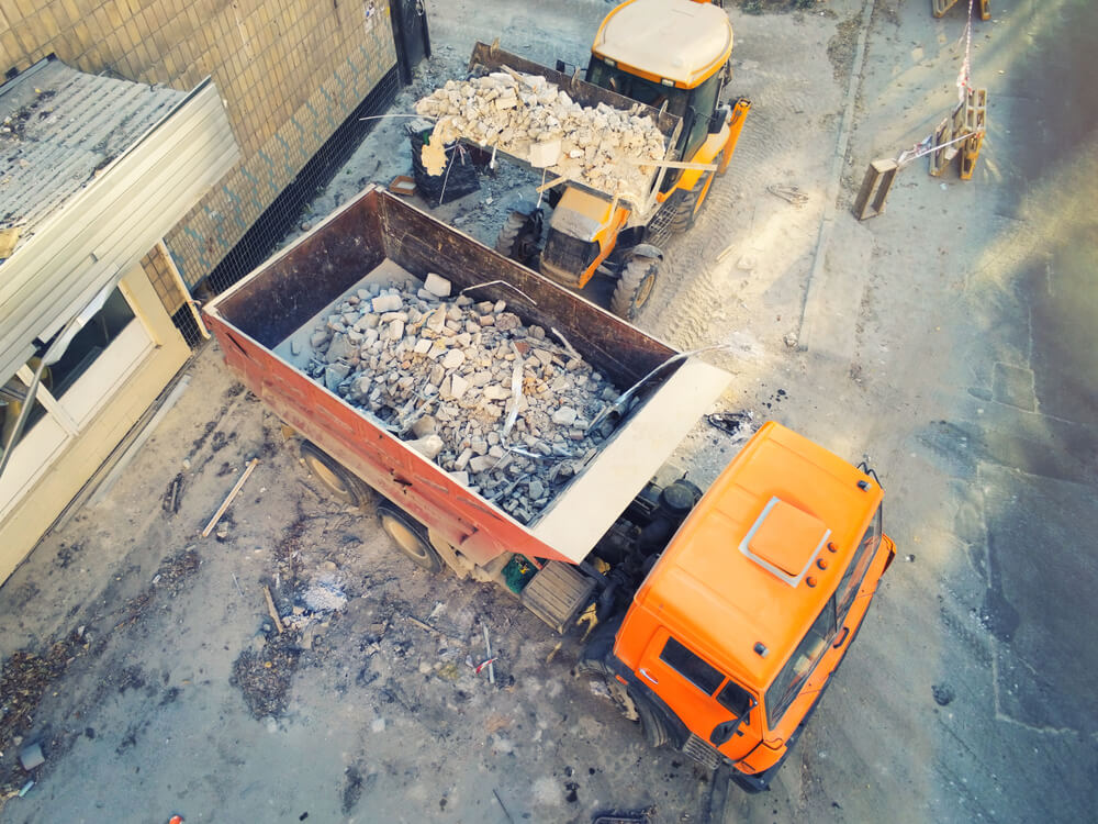 Bulldozer loader uploading waste and debris into a dump truck at the construction site.